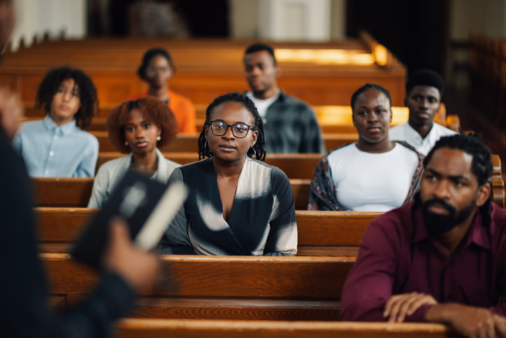 Group of Black church members attentively listening to a sermon from the pews
